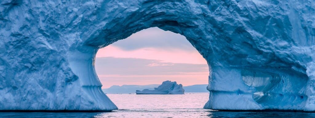 View through a natural ice cave overlooking the ocean at sunrise, symbolising transparency, perspective and resilience.
