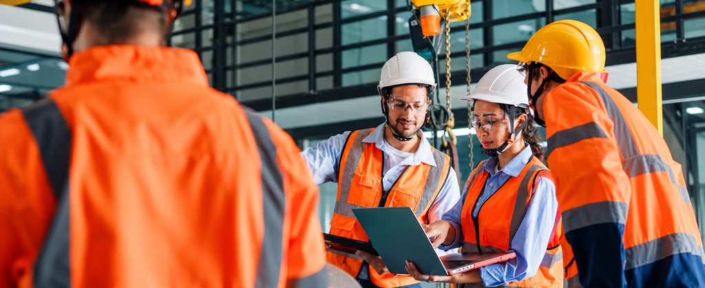 Workers wearing PPE reviewing documents and a laptop in an industrial facility.