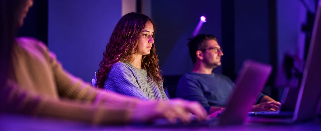 People working at computers in a cybersecurity training environment with purple lighting.