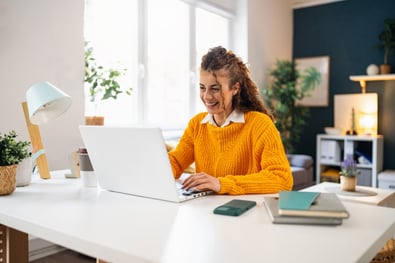 Woman smiling in orange jumper looking at her laptop