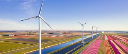 Wind turbines overlooking colourful agricultural fields, representing renewable energy and sustainable land use.