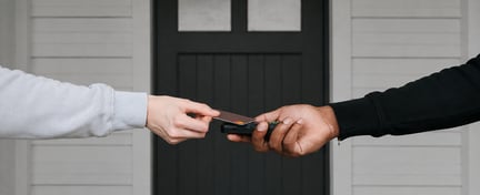 Contactless card payment being processed using a handheld payment terminal at a doorway.