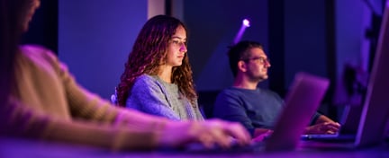 People working at computers in a cybersecurity training environment with purple lighting.