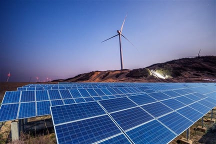 photo showing large scale solar panels and one windmill forming part of a windfarm