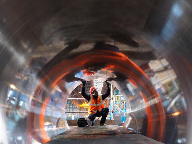 Industrial worker inspecting inside large metal pipe in manufacturing facility, demonstrating safety and quality assurance