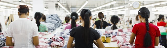 Trabajadores en una fábrica de confección clasificando y doblando telas sobre mesas grandes bajo luces intensas