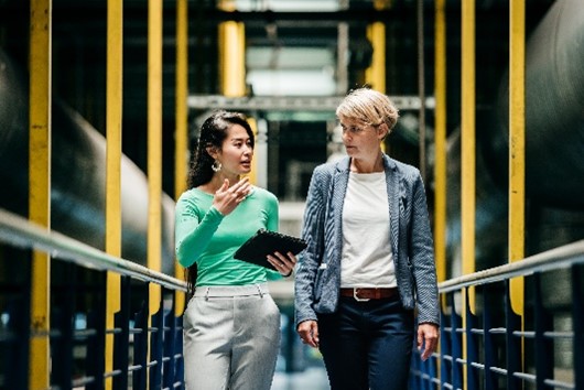 Duas profissionais conversando em instalação industrial enquanto analisam informações em tablet