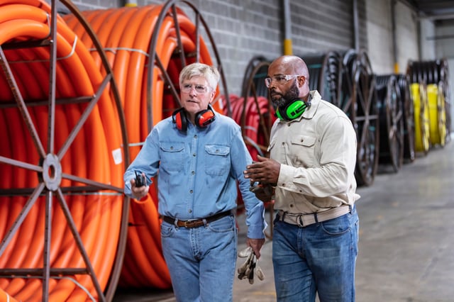 Two people talking in a warehouse with large cable rolls in the background