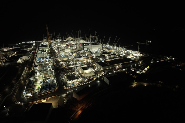 Night-time aerial view of an illuminated industrial facility by the coast.