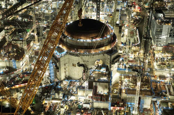 Night-time view of a large industrial construction site with cranes and reactor building.